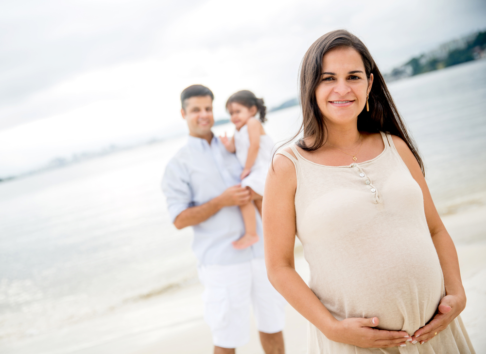 Pregnant woman at the beach with her family looking happy