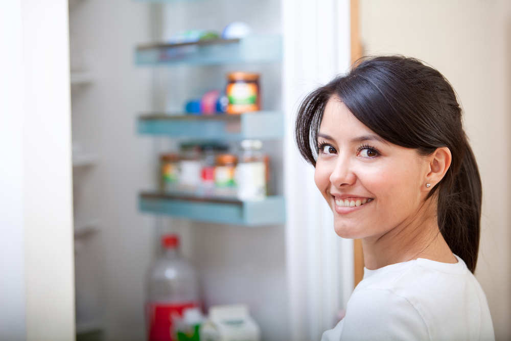 Woman at home looking inside the fridge and smiling